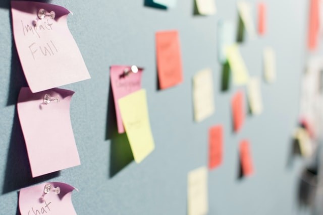 multiple, multi-colored sticky notes tacked on a blue board with writing that isn't quite legible