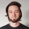 portrait of Derek Beaton standing in front of off-white wall