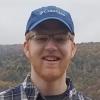 portrait of Nate Kratzer standing outside in front of a hill covered in trees